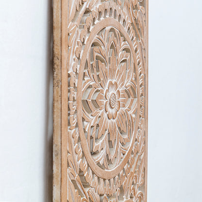 Close-up of a carved wooden wall panel with an intricate floral mandala design in a light natural wood finish against a plain white wall.