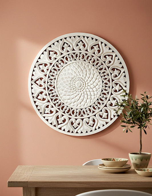 Decorative white wall art on a peach-colored wall with a wooden table and plant in the foreground.